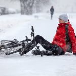 Fallen down Caucasian cyclist sitting on slippery roadside, riding bicycle in city at winter season